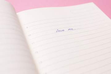 The inscription love me in a diary close-up on a pink background.