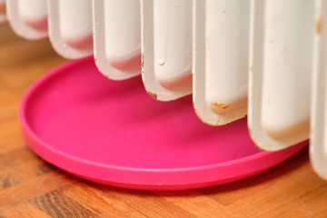 Old white leaking radiator in a living room with parquet floor and a pink plastic bowl ( turned around frisbee ) to collect the water that is dripping down. Seen in Germany in December