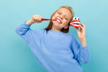 young european girl brushes her teeth on a light blue background