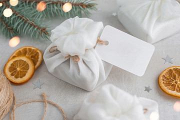 Obraz na płótnie Canvas Christmas presents wrapped with white furoshiki fabric, labels and dried orange slices. Eco friendly gift.