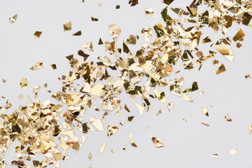Gold leaf confetti on white background. Festive, party or holiday glitter backdrop. Flat-lay, close-up. Diagonal spread.