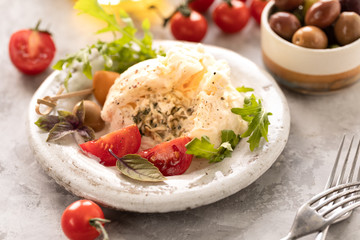 Burrata cheese with arugula and cherry tomatoes and olives on a round white plate on a light background close-up