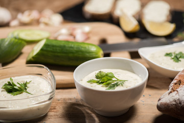 Selective focus of traditional greek tzatziki sauce with ingredients on wooden table