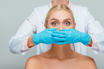 cropped view of beautician covering mouth of naked woman isolated on grey