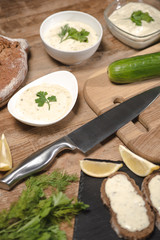 Tasty homemade tzatziki sauce with bread and greenery on wooden table