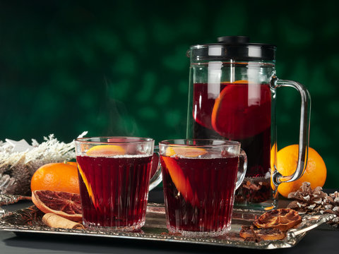 Mulled wine in a cafetiere or french press, with glasses on a silver tray, with pine cones and dried orange slices