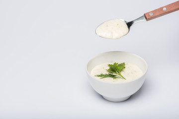 Tasty tzatziki sauce with greenery and spoon on white background