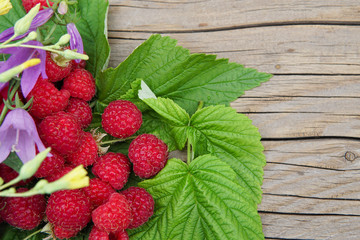 ripe raspberries with leaves and flowers on a wooden table.Space for text.