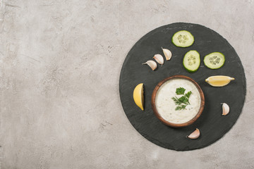 Top view of tzatziki sauce with vegetable and lemon slices on board on stone background