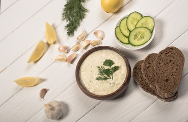 Top view of tzatziki sauce with greenery, cucumber and lemon on white wooden background