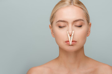 attractive and naked young woman with wooden pin on nose and closed eyes isolated on grey
