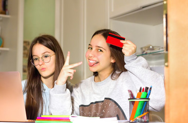 Two teen girls surf the Internet on their laptop, look for products of interest to them and make purchases with a credit card. Teenagers' concept of navigation, research and shopping