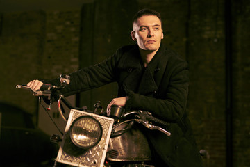 Man with black hair and black trench coat sitting on a motorbike