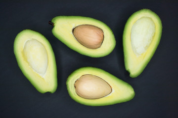 Halves of fresh ripe avocado. Avocado cut in half. With and without bone. On a dark gray background. Low key. Top view. Organic vegan or vegetarian food. Healthy fats, oil.