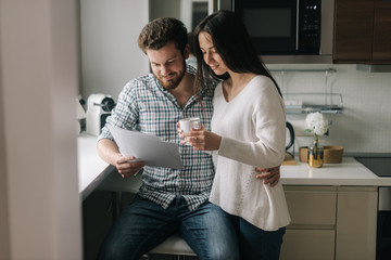 Serious married couple studying mortgage documents together. Beautiful girl holding a cup of coffee...
