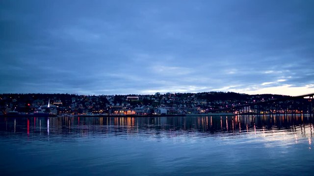 Tromso city, view of Tromso bridge, harbour and city centre from across the fjord, at night during blue hour light.