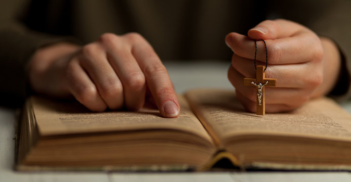 Reading God's commandments in the Bible, close-up of a hand with a crucifix.