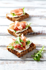 Tasty sandwiches with cream cheese, smoked ham and fresh herbs. Bright wooden background. 