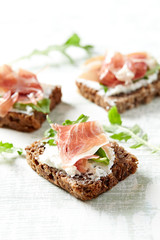 Tasty sandwiches with cream cheese, smoked ham and fresh herbs. Bright wooden background. Close up. 