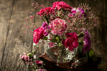 Bouquet of pink carnation in glass vase on old wooden background. Mothers day, birthday greeting card. Copy space.