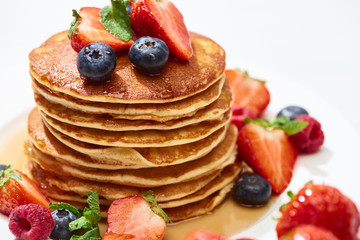 close up view of delicious pancakes with honey, blueberries and strawberries on plate on white surface