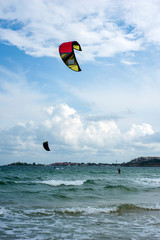 Kite surf ride his hydrofoil kite through surfing waves on sea.  Kitesurfers ride kites on Black Sea at sandy Beach In Bulgaria, Sozopol on sunny day at sunset on blue sky and clouds background.