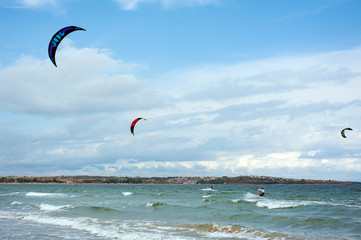 Kite surf ride his hydrofoil kite through surfing waves on sea.  Kitesurfers ride kites on Black Sea at sandy Beach In Bulgaria, Sozopol on sunny day at sunset on blue sky and clouds background.