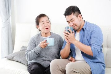 Asian senior grand mother and son drinking coffee and talking happy and smile face in living room