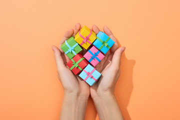 cropped view of woman holding multicolored small gift boxes on peach background