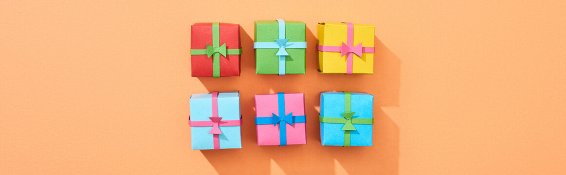 top view of multicolored small gift boxes on peach background, panoramic shot