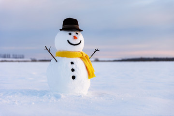 Funny snowman in stylish black hat and yellow scalf on snowy field. Merry Christmass and happy New...