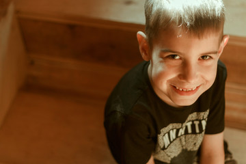 A boy in a black T-shirt sits on a wooden staircase and smiles. Sun's rays fall on him.