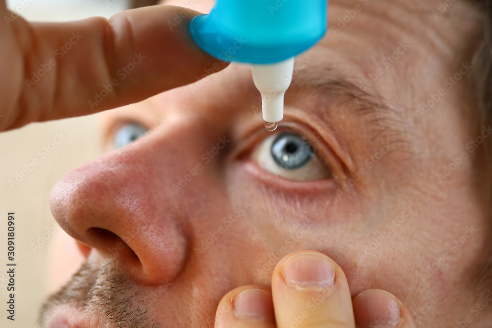 Wall mural male hand putting liquid drops in his eye