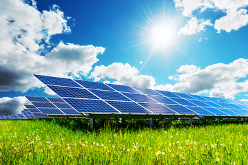 Solar panel under blue sky with sun. Green grass and cloudy sky. Alternative energy concept