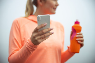 Fototapeta premium Young woman holding modern smartphone and bottle of water