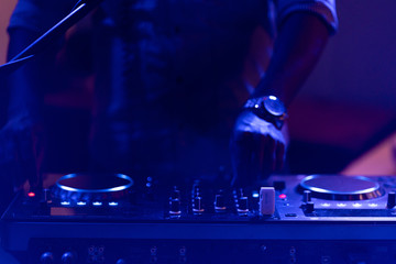 club dj plays music on stage in nightclub.Hand of disc jockey adjusting sound track volume...
