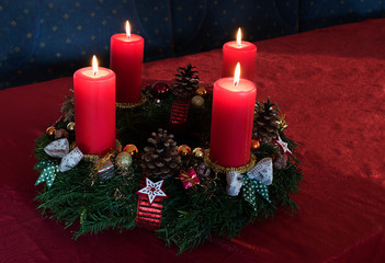 advent wreath with four lighted red candles on a claret tablecloth