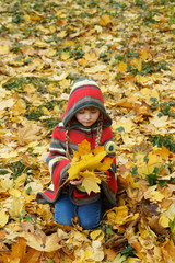 cute charming baby vertical portrait with a bouquet of autumn leaves and a wreath walking outdoors in a park or forest, dressed in a warm knitted bright poncho