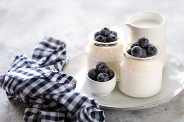 Milk and homemade yogurt in a jar on a white plate. Whipped cream with blueberries as a dessert in two glass jars.