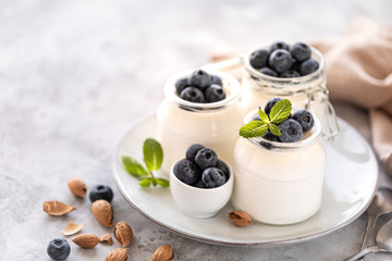 Non-dairy alternative. Vegetable yogurt in jars on a white background. Almond and oat cream in a glass jar and fresh blueberry on a light plate and almond bones with sprigs of oats. 