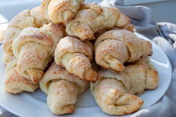 Ruddy sugar-frosted croissants from a curd dough lying on a white plate next to a gray cloth. Sweet baked bagels just taken out of the oven. A delicious tea snack for breakfast