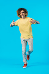 curly teenager pointing with fingers at himself isolated on blue