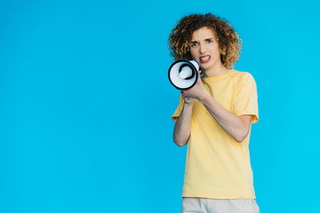Fototapeta premium angry curly teenager screaming in loudspeaker isolated on blue