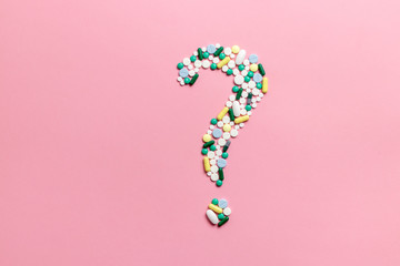 Composition of pills and capsules on a pink background in the form of a question mark....