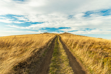 highland valley dry yellow grass land on mountain ridge top with dirt road ho horizon background in autumn moody atmospheric weather time