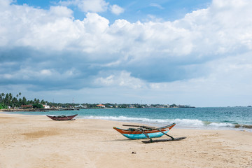 Fototapeta na wymiar Old catamaran boats on the beach against the ocean and blue sky with beautiful clouds on a sunny day, Sri Lanka