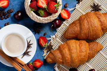 Obraz na płótnie Canvas Croissant with fresh berries and coffee cup at blue table top view. 