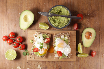 bread slice with avocado, poached egg, tomato and cheese on wooden board