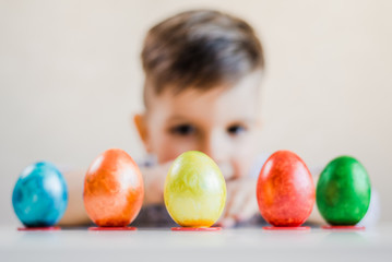 Fototapeta na wymiar Multi-colored Easter eggs stand in a row on stands on the background of a boy looking at them.