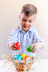 Fototapeta na wymiar Happy little boy with a smile lays Easter eggs in a basket on a table on a white background.